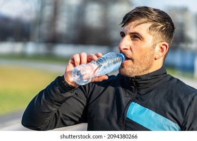 Close Up Portrait Of Adult Caucasian Man Standing Outdoor With Plastic Bottle Of Water Drinking - Male Amateur Athlete Drink During Rest At Outdoor Training In Sunny Day - Real People Copy Space