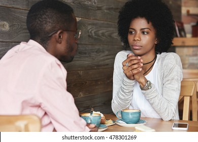 Close up portrait of African American friends at cafe having serious conversation, fashionable hipster woman with Afro hairstyle looking at her boyfriend with puzzled and thoughtful face expression - Powered by Shutterstock