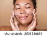 Close up portrait of african american young woman applying a scrub skin care mask on her face. Skincare exfoliating dermatology procedure 