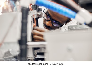 Close up portrait of african engineer working with wires and curcuits at factory, repairing LED lamps production line, connecting wires, fixing equipment. He is wearing white robe and glasses