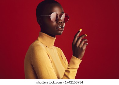 Close up portrait of african female with buzz cut hairstyle against red background. Beautiful african woman in casuals wearing sunglasses looking at camera.