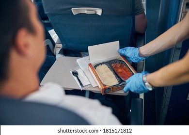 Close Up Portrait Of Air Stewardess Serving Box Of Food For Male Passenger In Protective Gloves To Prevent Covid Virus Affection In Airplane Cabin