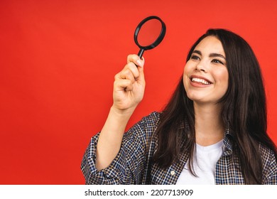 Close Up Portrait Of Amazing Beautiful Woman Looking At Camera Through Magnifying Glass, Isolated On Red Background. Having Fun.