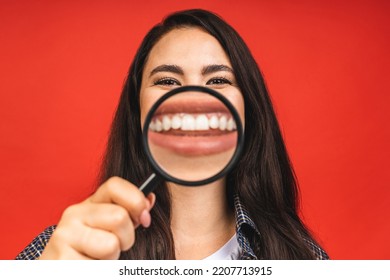 Close Up Portrait Of Amazing Beautiful Woman Looking At Camera Through Magnifying Glass, Isolated On Red Background. Having Fun.

