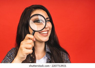 Close Up Portrait Of Amazing Beautiful Woman Looking At Camera Through Magnifying Glass, Isolated On Red Background. Having Fun.