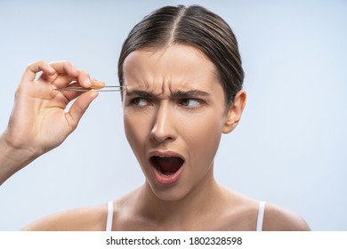 Close Up Portrait Of An Angry Caucasian Lady Plucking Her Eyebrows With A Pair Of Tweezers