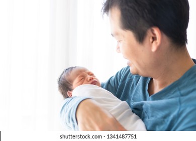 Close up portrait of asian young father is hugging and looking to his newborn baby boy with fully happy moment, concept of love and bonding in the family lifestyle, selective focus photography.