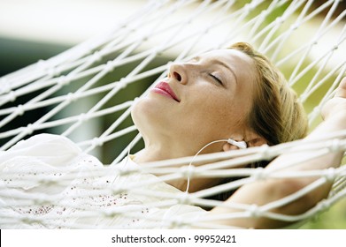 Close Up Portrait Of An Attractive Blonde Woman Laying Down On A Hammock Listening To Music, With Her Eyes Closed And Smiling.