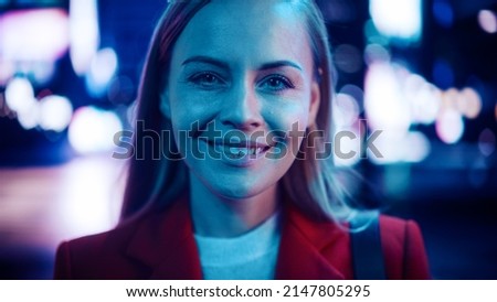 Close Up Portrait of an Attractive Caucasian Woman Smiling, Looking at Camera, Standing in Night City with Blue Neon Street Lights. Happy Confident Young Female with Blond Hair and Blue Eyes.