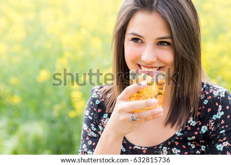 Close up portrait of attractive girl drinking ice tea outdoors against yellow flower background.