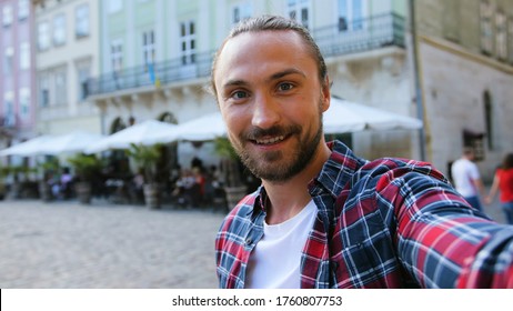 Close up portrait of attractive man with beard possing on camera while making photo or video on the city background.