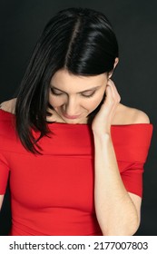 Close Up Portrait Of Attractive Middle-aged Woman With Dark Hair And Eyes, Looking Down And Touching Hair, Wearing Red Dress With Opened Shoulders. Smoky Make Up. Black Background.