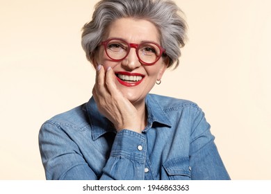 Close up portrait of attractive senior woman in modern red eyeglasses. Happy older female teacher with trendy haircut and toothy smile on beige background. Eyesight problem and stylish eyewear