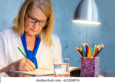 Close Up Portrait Of Attractive Senior Woman Doing Color Therapy With Coloring Book For Adults.Woman Sitting At Table Drawing.