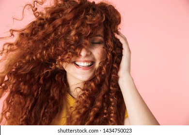 Close Up Portrait Of An Attractive Smiling Happy Young Woman With Long Curly Red Hair Standing Isolated Over Pink Background