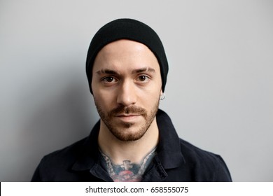 Close up portrait of attractive tattooed man. Head shot of stylish guy, who look to the camera. Caucasian male on grey background looking serious. - Powered by Shutterstock