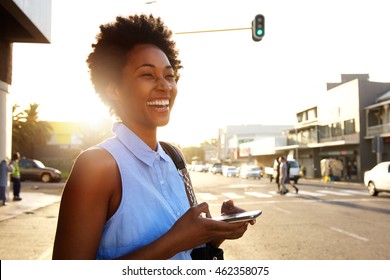 Close up portrait of attractive woman with mobile phone looking away and laughing on the city street