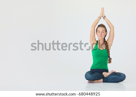 Close up portrait of attractive woman sitting in meditating position on white floor. Young girl raising hands doing yoga.
