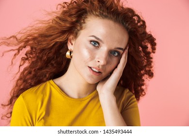 Close Up Portrait Of An Attractive Young Woman With Long Curly Red Hair Standing Isolated Over Pink Background