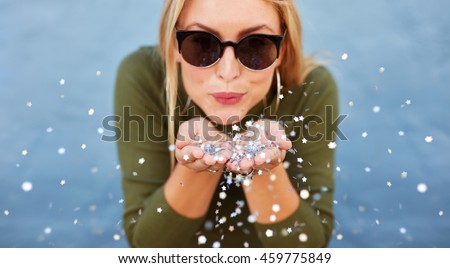 Close up portrait of attractive young woman blowing glitters. Caucasian Female model having fun over blue background.