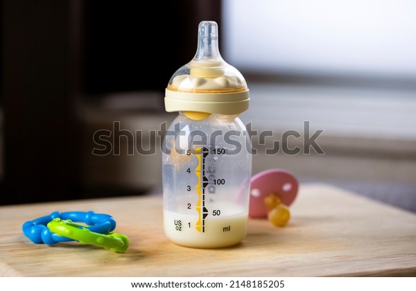 A close up portrait of a baby bottle with a bit of\
formula still in it standing on a wooden plank. The glass nursing\
bottle still has some milk in it and has a rubber dummy nipple, or\
bottle teat. 
