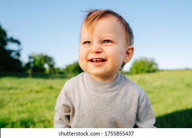 Close Up Portrait Of Baby Boy Over Countryside. He Has Weird Face Expression. Blurred Surroundings.