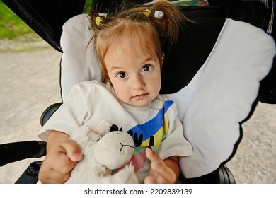 Close Up Portrait Of Baby Girl Hold Toy In Sitting Stroller. 