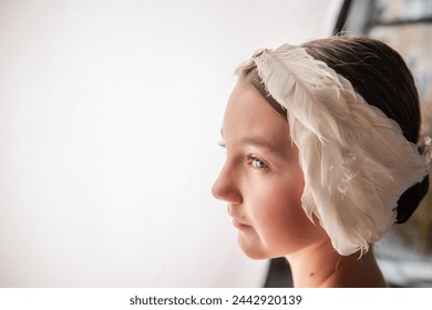 Close up portrait of Ballerina Dreamscape. Young girls moment of repose, face lit by natural light, as rests by a window adorned with a feathered headpiece. - Powered by Shutterstock