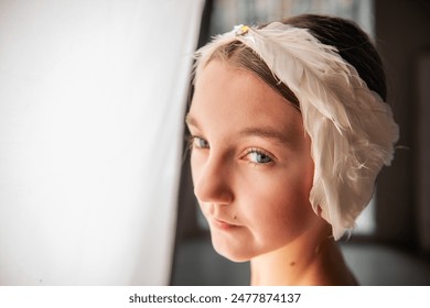 Close up portrait of Ballerina Dreamscape. Young girls moment of repose, face lit by natural light, as rests by a window adorned with a feathered headpiece. - Powered by Shutterstock