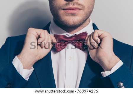Close up portrait - bearded man ties a bowtie at the collar, correcting red bow on his white shirt over grey background