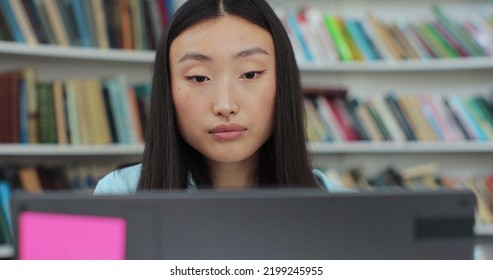 Close Up Portrait Beautiful Asian Girl In Reading Book And Typing On Computer. College Student Works On Essay At The Library.