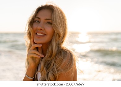  Close up portrait of beautiful blond woman in sexy swimwear posing on the beach in sunset light. Prtfect wavy hairs, tan skim body. Summer tropical mood. 