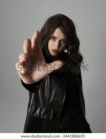 close up portrait of beautiful brunette woman wearing long black leather trench coat. Gestural hand poses, arms reaching towards camera, with wide angel perspective, Isolated on studio background