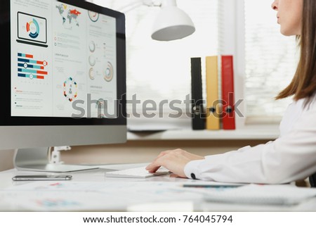 Close up portrait of the beautiful business woman in suit working at computer with documents in light office, looking at the monitor, hands on the keyboard