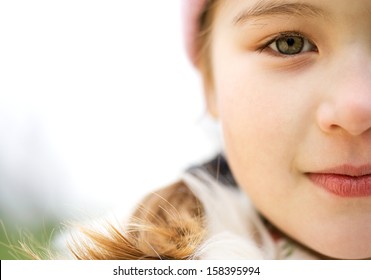 Close Up Portrait Of A Beautiful Child Girl Half Face In A Park Looking At Camera And Being Thoughtful During A Cold Winter Day, Wearing A Warm Coat And A Pink Hat, Outdoors.