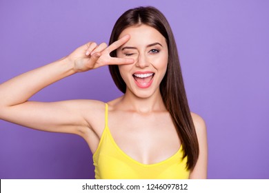 Close up portrait of beautiful dreamy attractive pretty gorgeous charming lovely lady in her yellow top make toothy smile she show v-sign near wink eye isolated on shine purple background