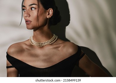 Close Up Portrait Of A Beautiful Elegant Young Woman Wearing An Expensive Pearl Necklace, Pearl Earrings In A Black Evening Dress.