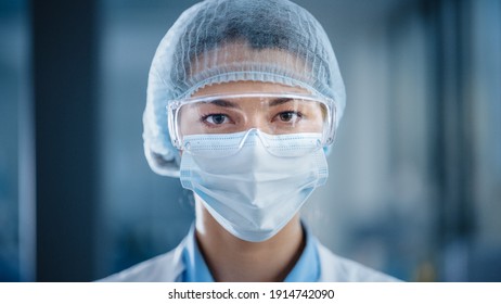 Close Up Portrait of a Beautiful Female Doctor or Surgeon Wearing a Protective Face Mask, Goggles and Disposable Surgical Cap. Laboratory Scientist Calmly Looking at Camera. Covid-19 Pandemic Concept. - Powered by Shutterstock