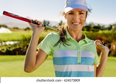 Close up portrait of beautiful female golfer holding golf club on field. Young woman standing on golf course and smiling. - Powered by Shutterstock