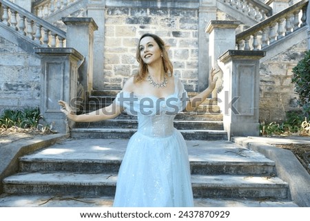 Close up  portrait of beautiful female model wearing blue fantasy ballgown, like a fairytale elf princess.  Elegant pose, gestural hands reaching out, on the terrace of a romantic castle staircase 