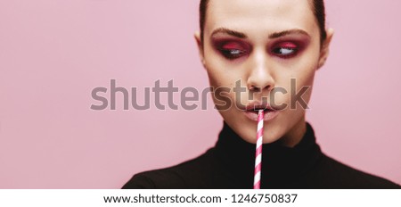 Close up portrait of beautiful female with a straw looking away. Fashionable woman on pink background looking at side with straw in mouth.