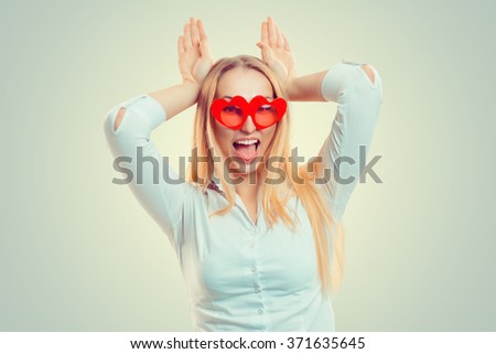 Close up portrait of beautiful happy excited young woman with heart shaped red glasses hands on head playing partying isolated green yellow background wall. Positive human emotion body language. Party