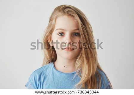 Close up portrait of beautiful little girl with light long hair and big blue eyes looking in camera with relaxed expression.
