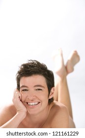 Close Up Portrait Of A Beautiful Mature Woman Laying Down Naked, Isolated Against A White Background, Smiling At Camera.