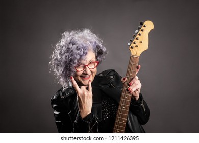 Close Up Portrait Of Beautiful Older Woman Holding An Electric Guitar On A Gray Background