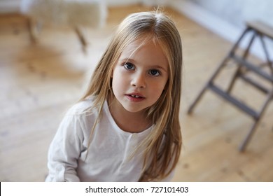 Close up portrait of beautiful pretty 5-year old Caucasian girl with big eyes and long straight hair posing indoors, looking at camera with curious interested expression on her face. Happy childhood