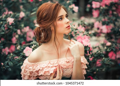 Close up portrait of a  beautiful red hair girl in a pink vintage dress standing near colorful flowers. Art work of romantic woman .Pretty tenderness model looking at camera.