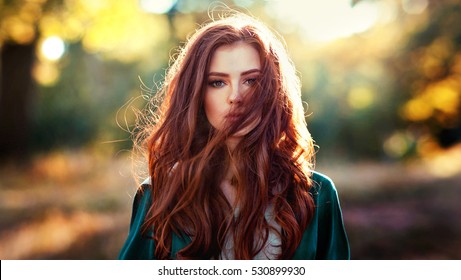 Close up portrait of  a beautiful red haired girl in green medieval dress on glowing sun. Fairy tale story about brave heart woman.Amazing model looking at camera.Warm art work
