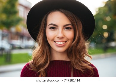 Close up portrait of a beautiful smiling girl with brown hair wearing a hat and looking at camera outdoors