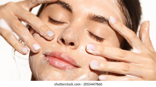 Close up portrait of beautiful woman clean her skin with cleansing gel, washing face and smiling from pleasure, standing over white background - Shutterstock ID 2055447860